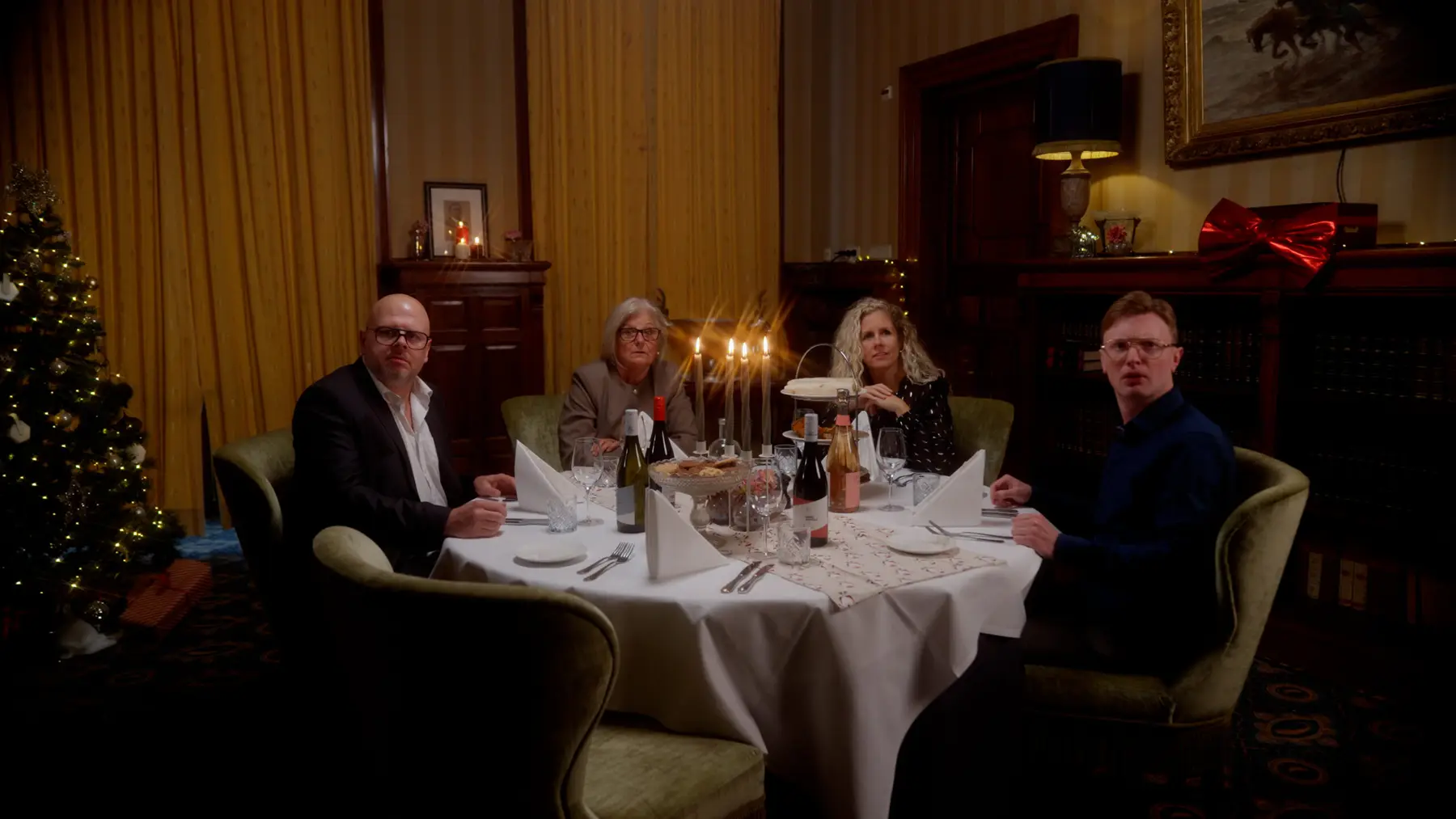 Vier mensen aan een feestelijk gedekte tafel met kaarslicht in een sfeervolle eetkamer.