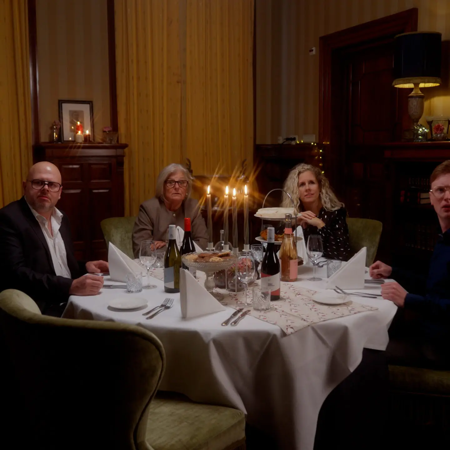 Vier mensen aan een feestelijk gedekte tafel met kaarslicht in een sfeervolle eetkamer.