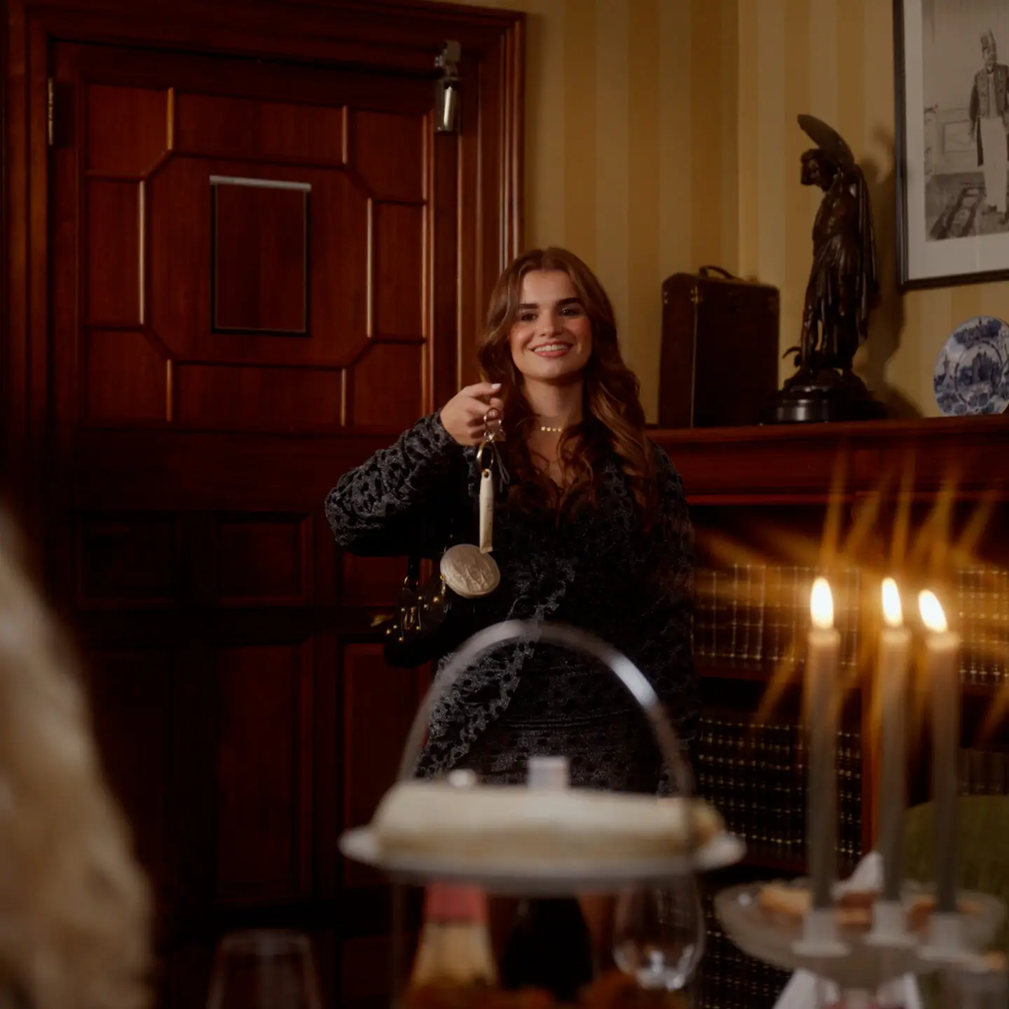 Een vrouw aan een gedekte kersttafel met kaarsen, in een klassiek interieur met warm licht.