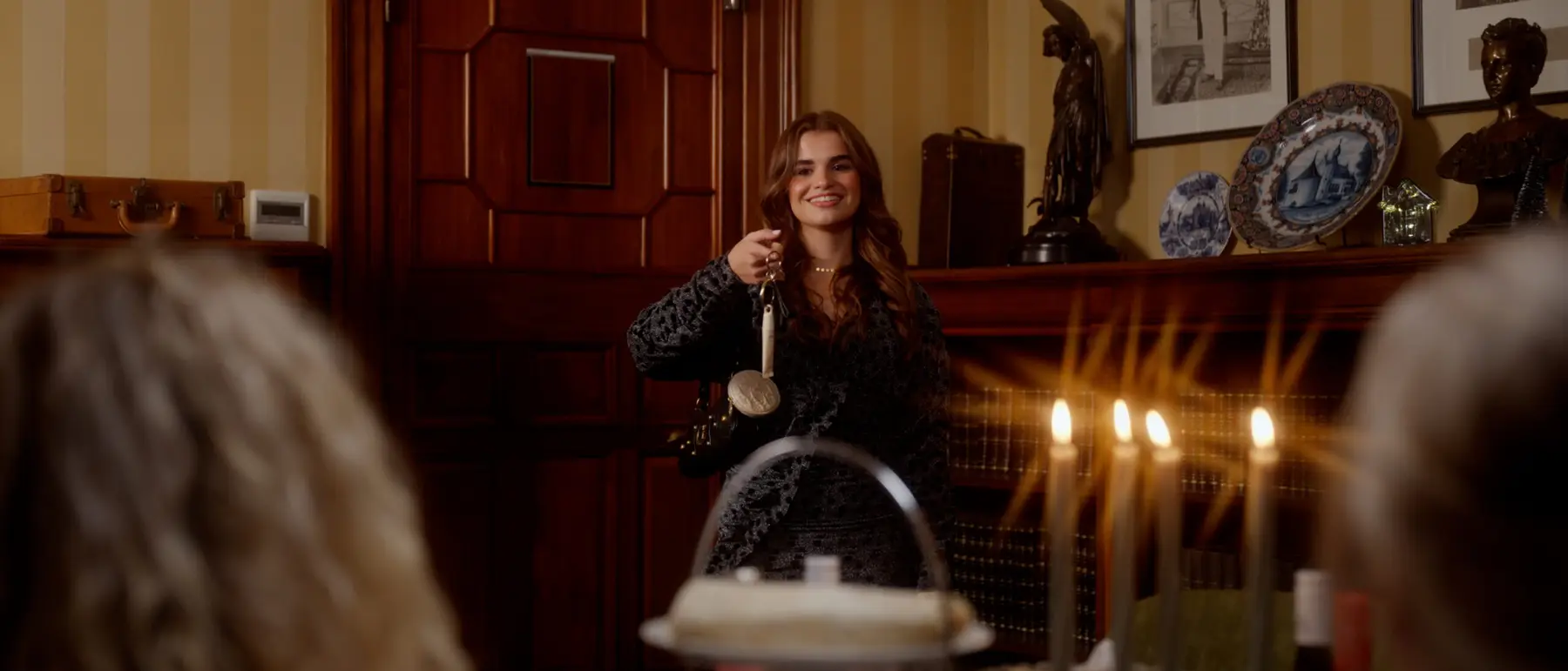 Een vrouw aan een gedekte kersttafel met kaarsen, in een klassiek interieur met warm licht.