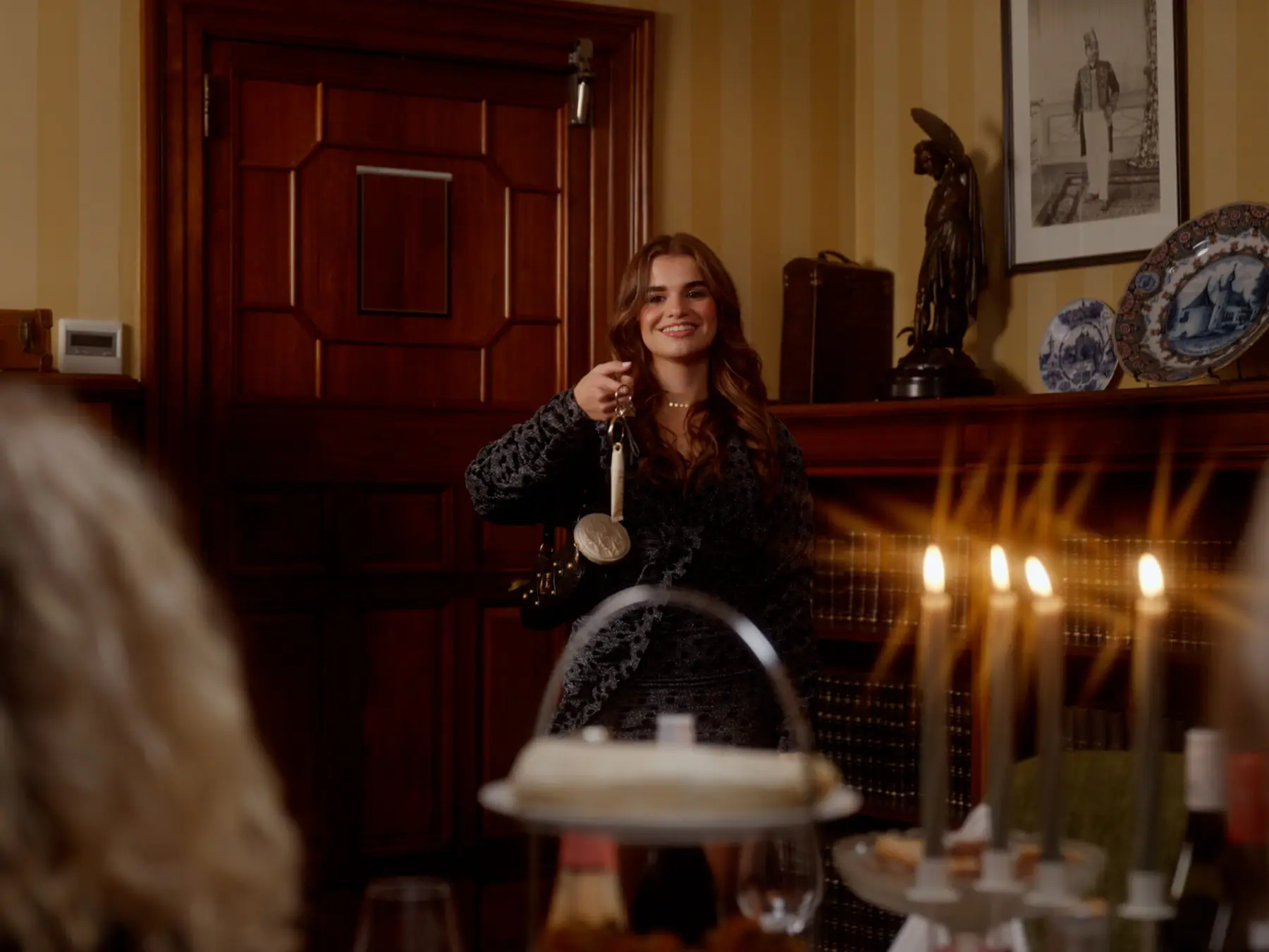 Een vrouw aan een gedekte kersttafel met kaarsen, in een klassiek interieur met warm licht.