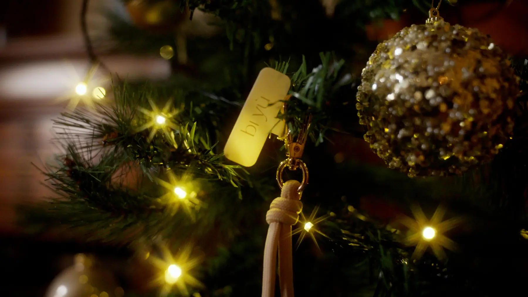 Close-up van een label van bi yù tussen kerstlichtjes en een glinsterende kerstbal.