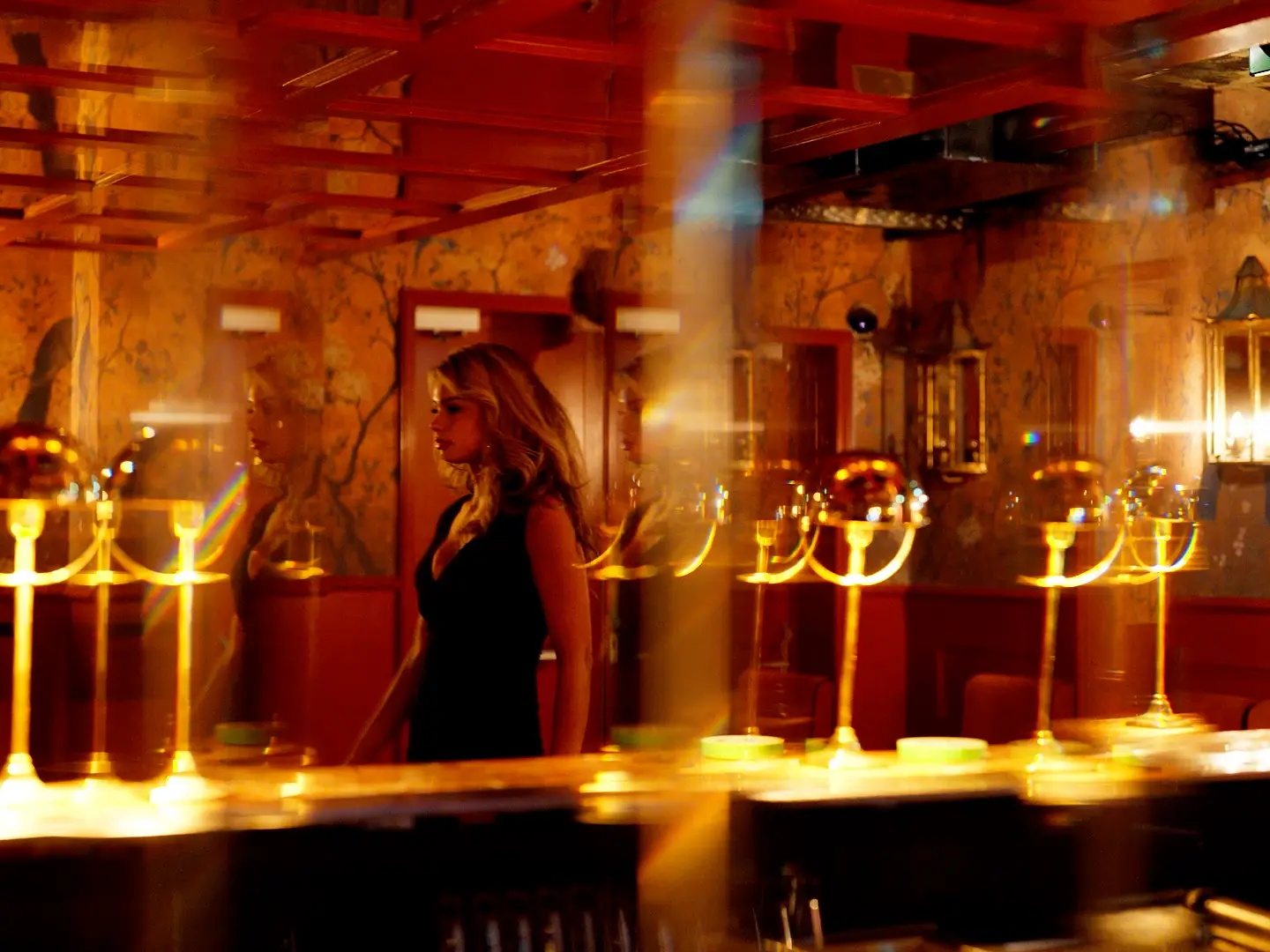 Een lange bar met gouden lampen en een vrouw in het midden van een warm verlichte ruimte.