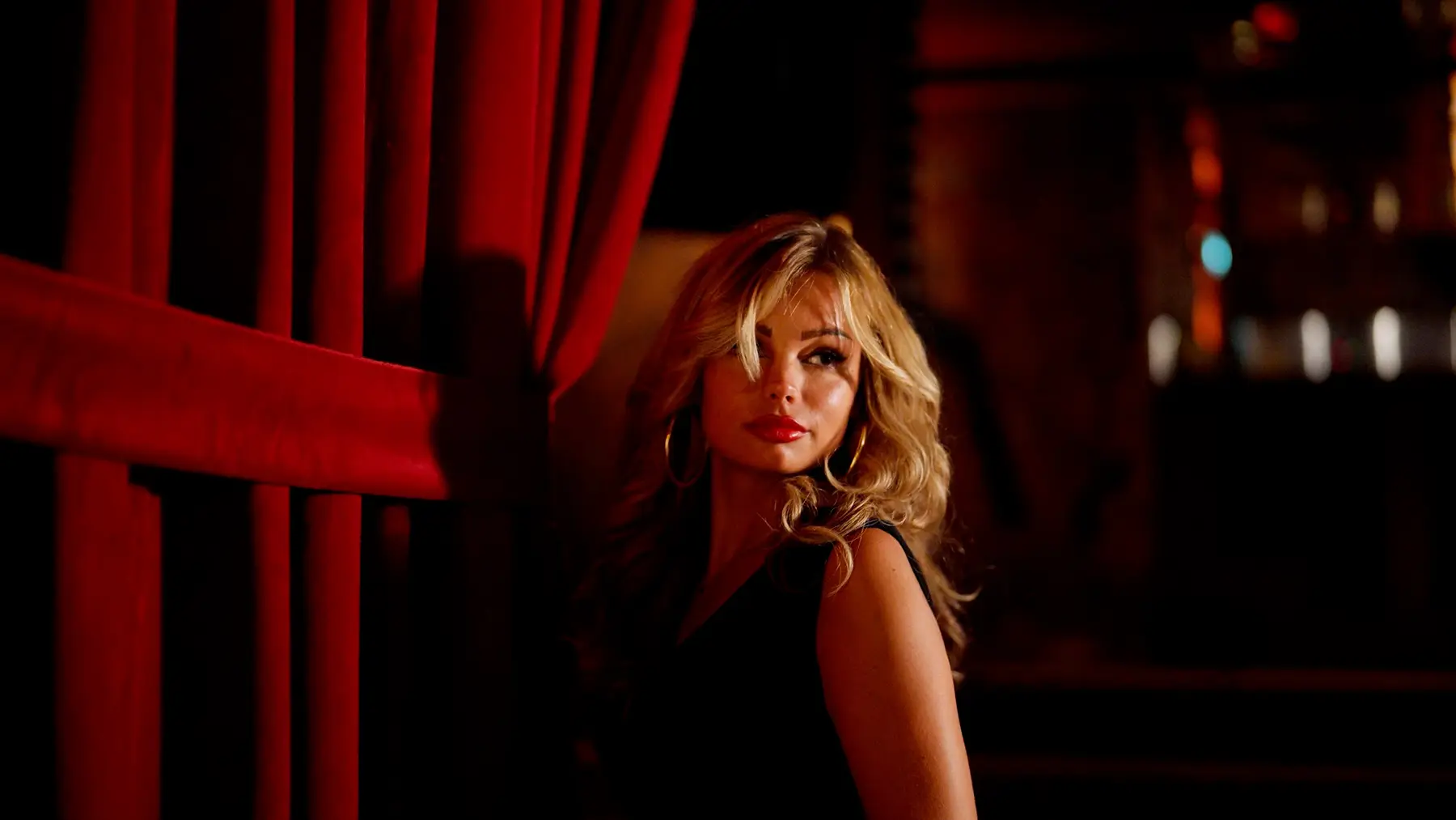 Portret van een vrouw met blond haar tussen rode gordijnen, uit de content voor Cîroc × Chin Chin Club.