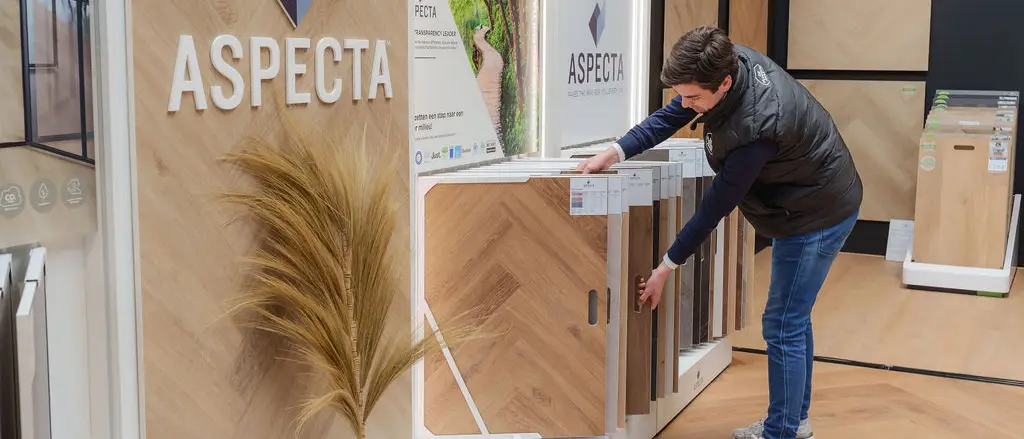 Een medewerker trekt een vloerpaneel uit een wandpresentatie in een lichte showroom.