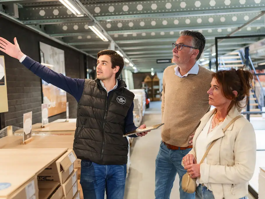 Een medewerker van De Vloerenzaak wijst een stel iets aan in de lichte showroom.