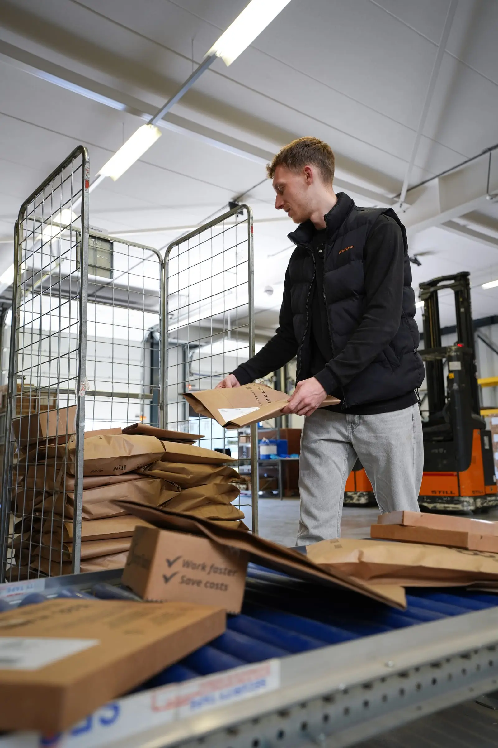 Een medewerker pakt dozen uit op een lopende band in het magazijn.