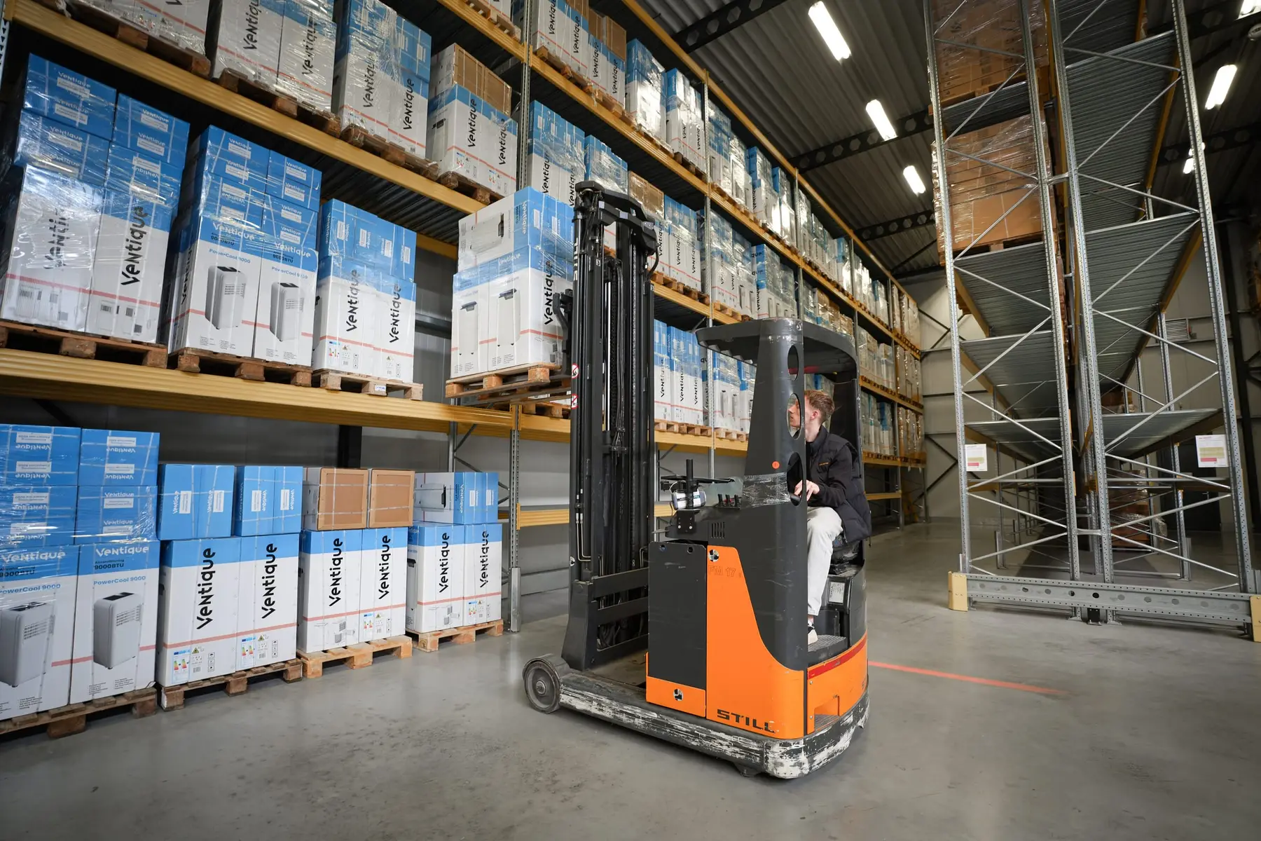 Een medewerker rijdt op een reachtruck door een gang met stellingen vol dozen.