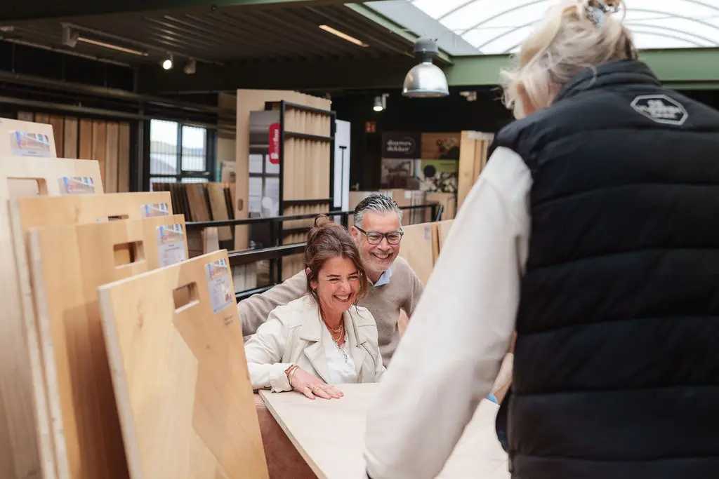Een stel bekijkt lachend houten vloerdelen aan een tafel in de showroom.