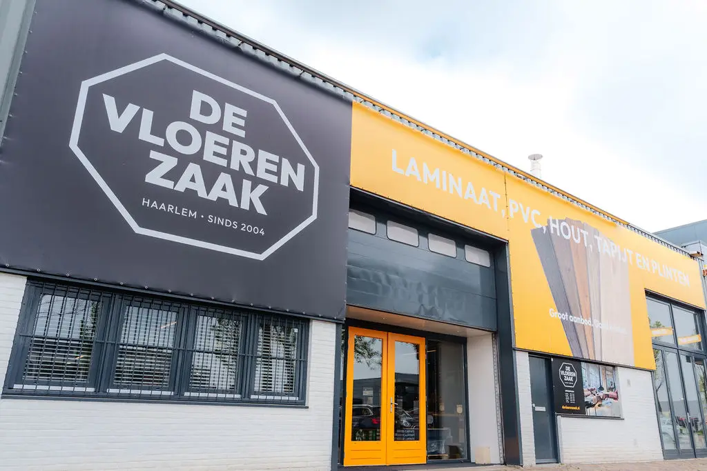 De gevel van De Vloerenzaak in Haarlem, met een groot zwart-wit logo en gele belettering.