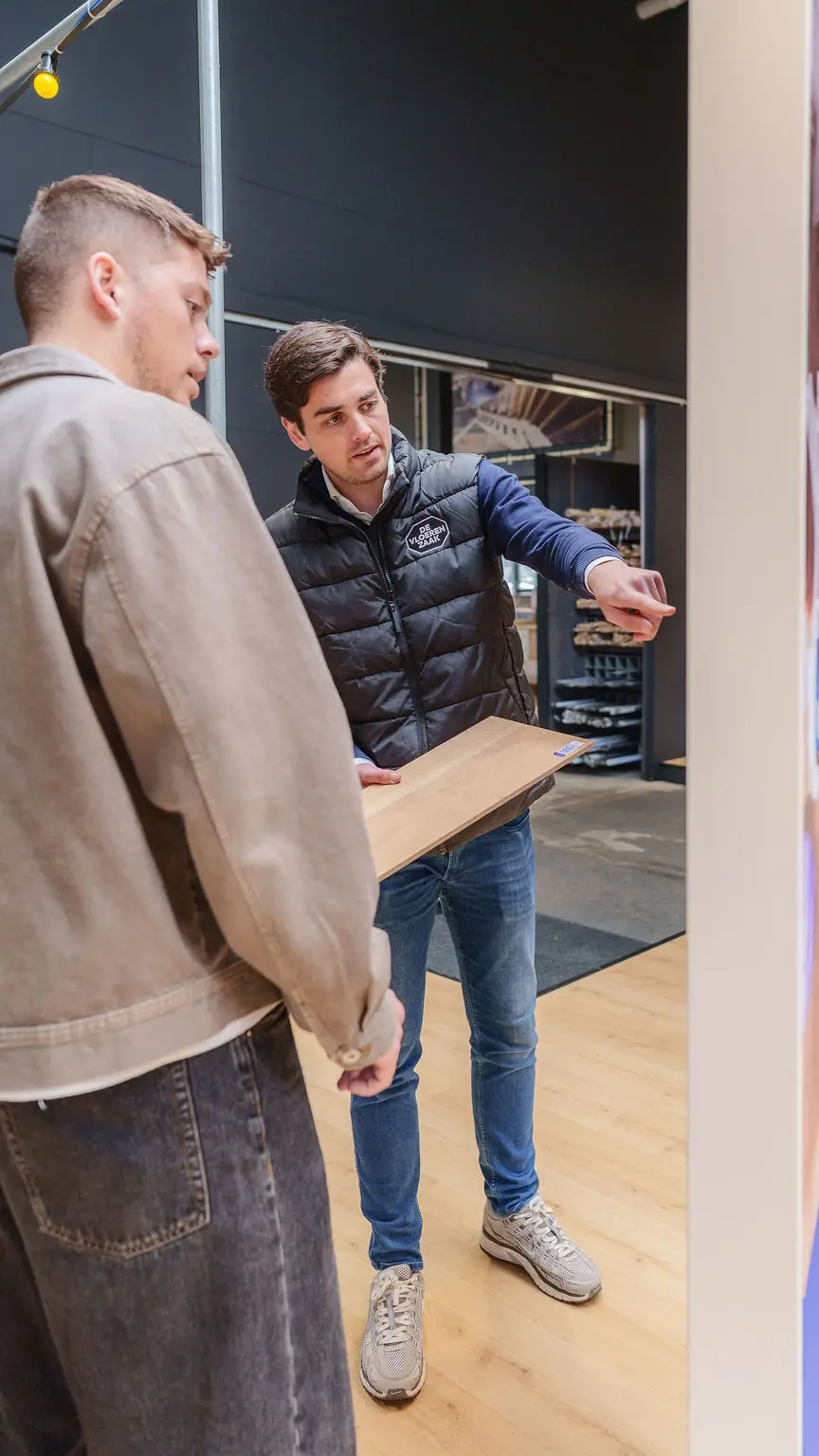 Een medewerker van De Vloerenzaak laat een klant een vloerdeel zien in de showroom.