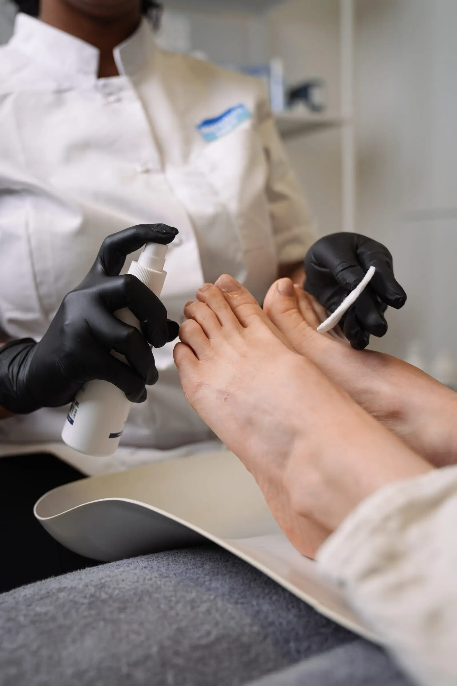 Een pedicure in zwarte handschoenen brengt een product aan bij een teen.