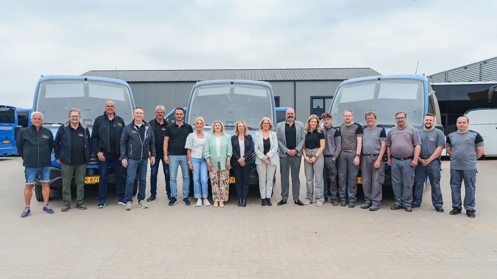 Het team van AB-BC staat in een lange rij voor drie bussen.