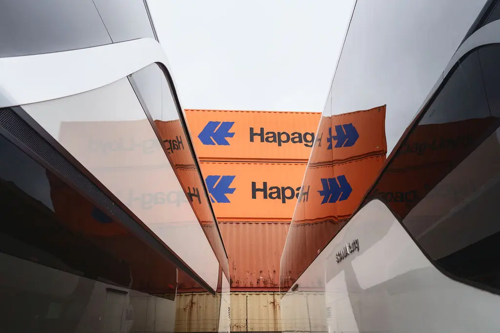 Gestapelde containers tussen de spiegelende neuzen van twee touringcars.