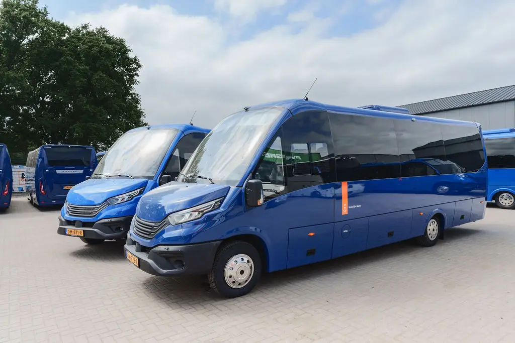 Twee blauwe minibussen staan geparkeerd op een terrein onder een bewolkte lucht.