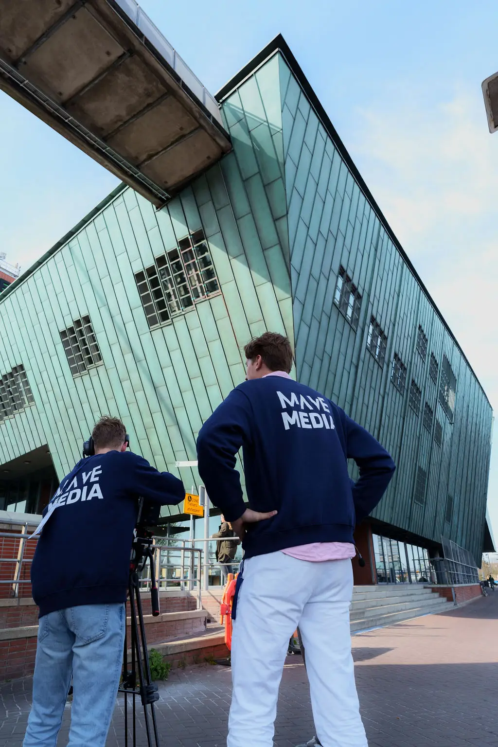 Twee crewleden met camera voor een groen, schuin gebouw.