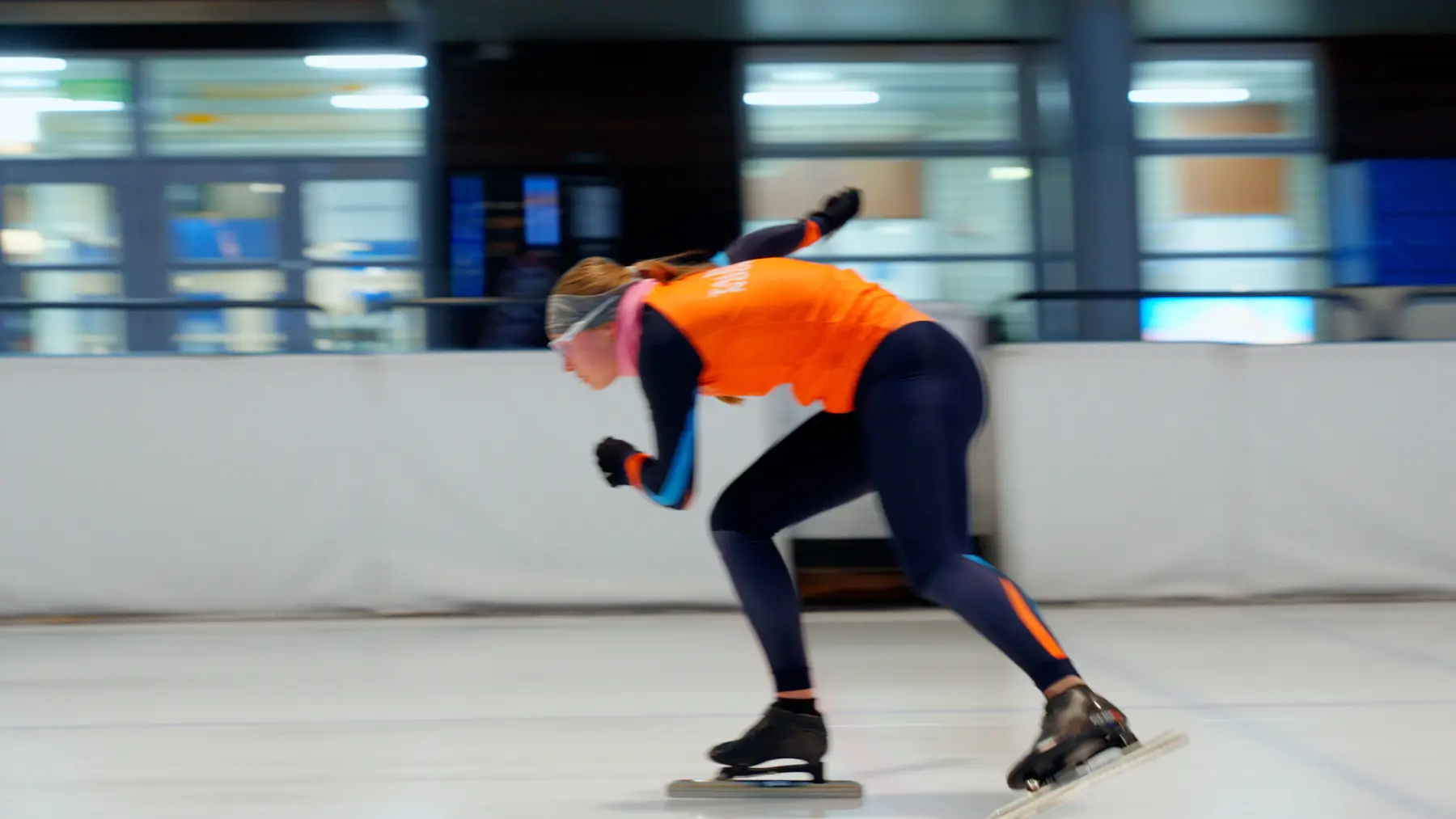 Een schaatser in oranje pak schaatst laag en snel voorbij.