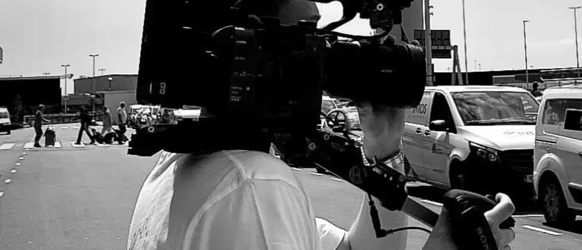 Zwart-witfoto van een cameraman met een schoudercamera op straat.