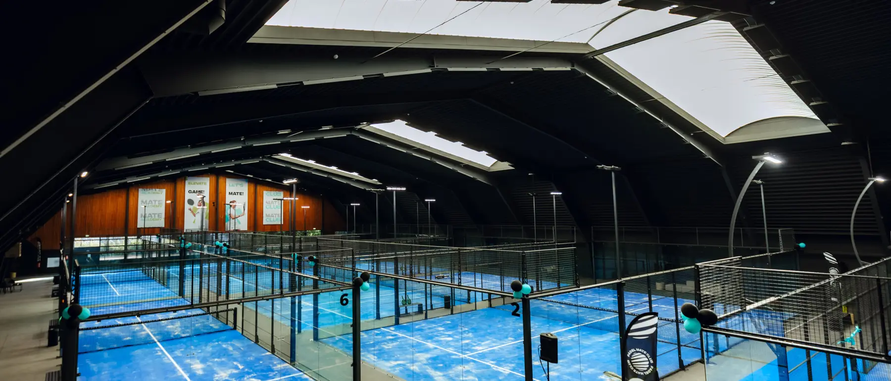 Overzicht van een overdekte padelhal met blauwe banen, gezien van bovenaf.