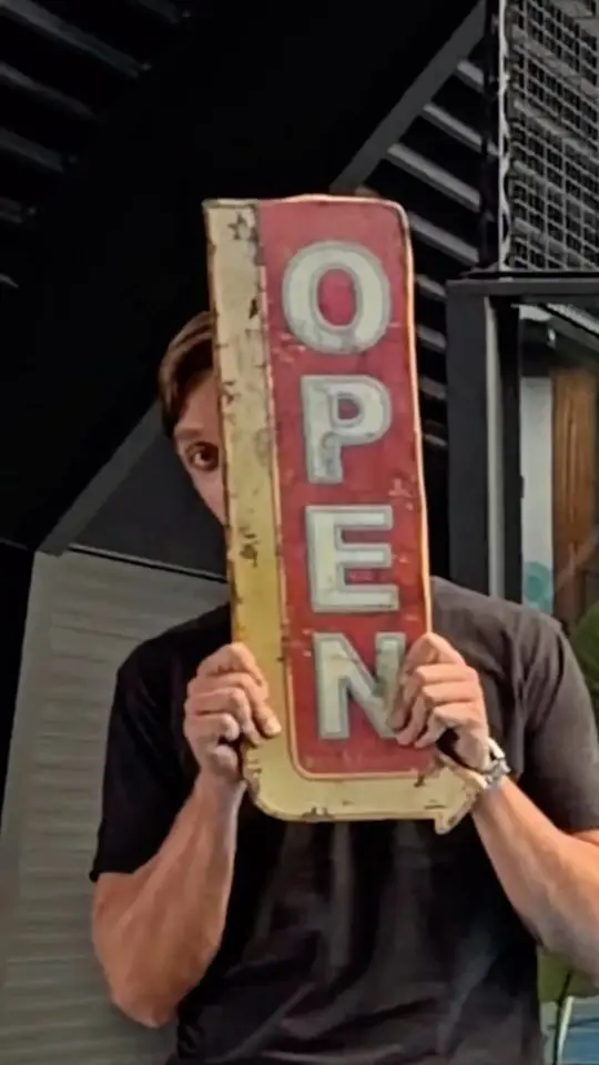 Reelcover van Padel Mate Club: een man houdt een rood bord met OPEN voor zijn gezicht.