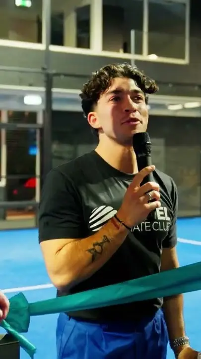 Een man met microfoon bij de opening van een padelclub, naast een lint.