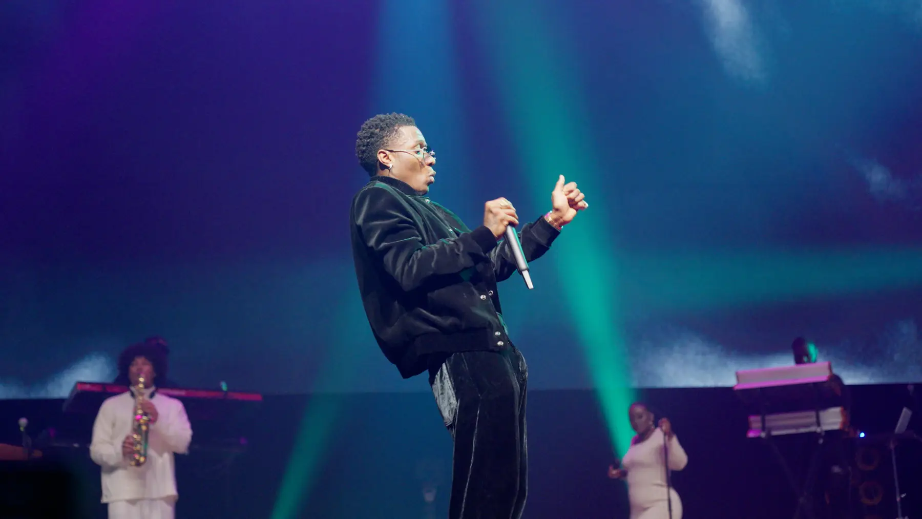Wizkid zingt in een groene lichtbundel, met een saxofonist op de achtergrond.