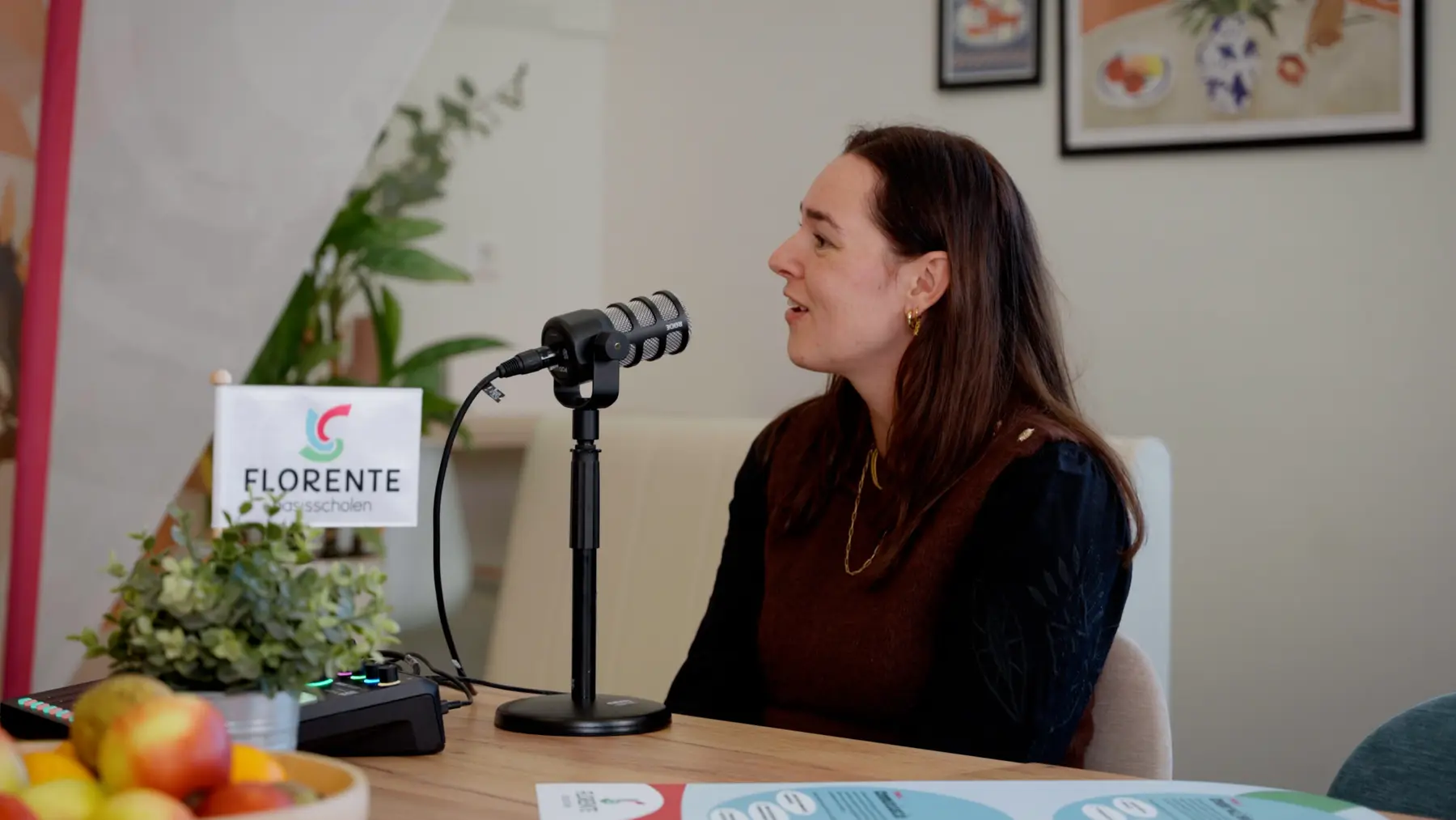 Een vrouw spreekt in een microfoon, met een Florente-bordje op tafel.