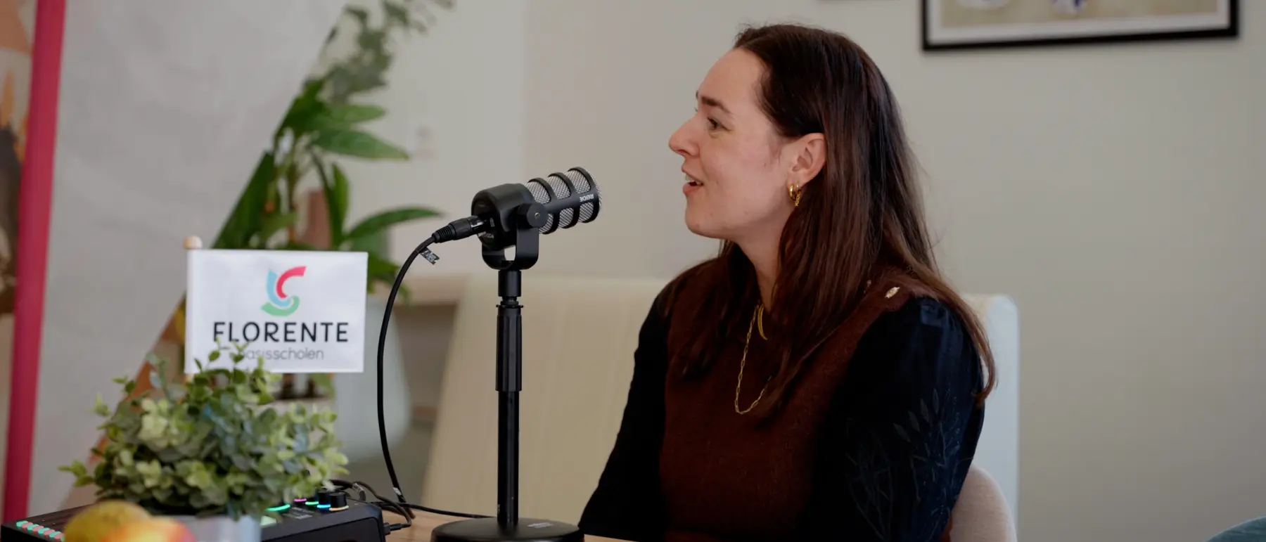 Een vrouw spreekt in een podcastmicrofoon, met een naambordje op tafel.