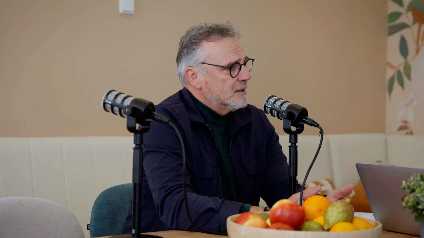 Een man met bril vertelt achter een podcastmicrofoon.