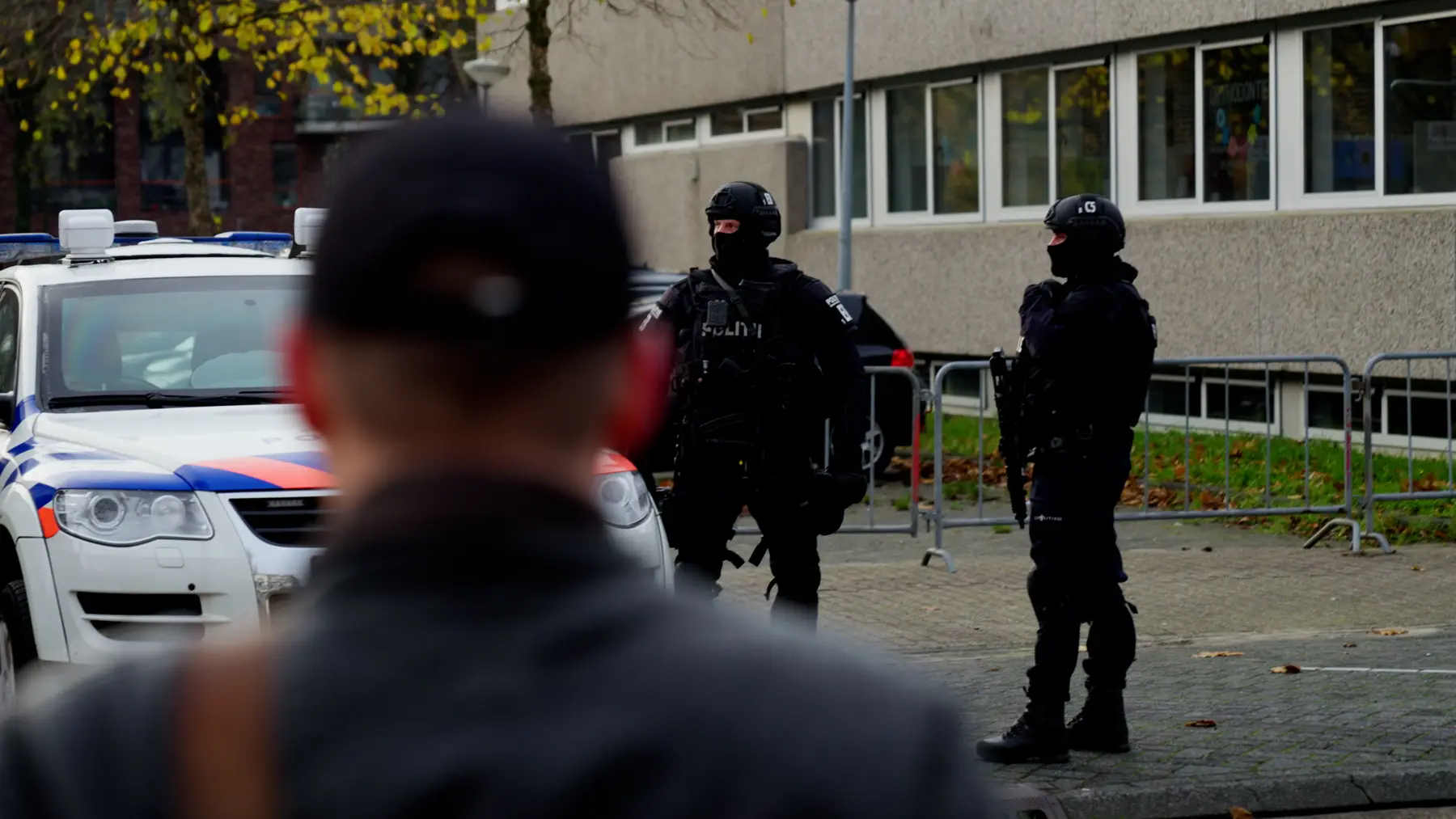 Over de schouder van een man gezien: twee agenten van een arrestatieteam bij een gebouw.
