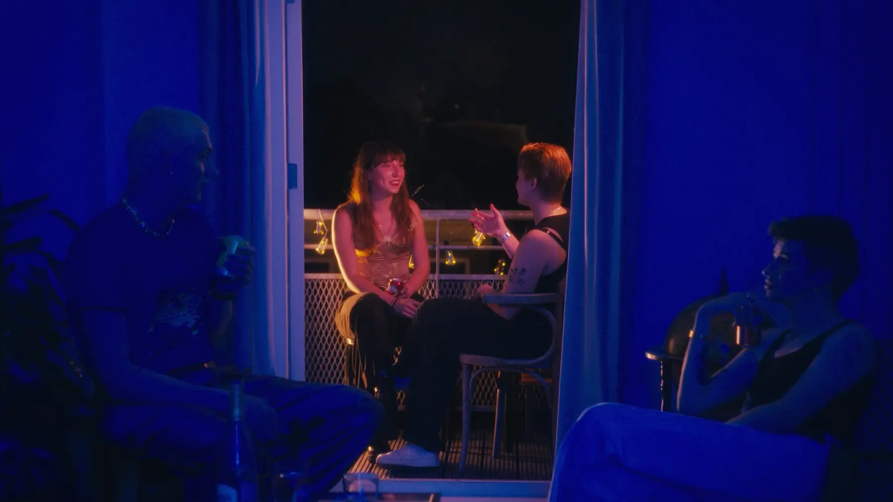 Twee vrienden praten op een bank in een blauw verlichte ruimte; op de voorgrond zitten anderen in silhouet.