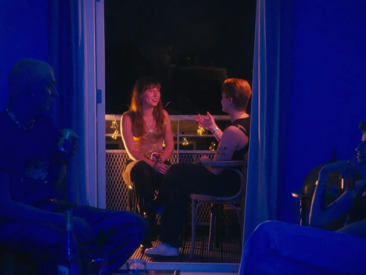 Twee vrienden praten op een bank in een blauw verlichte ruimte; op de voorgrond zitten anderen in silhouet.